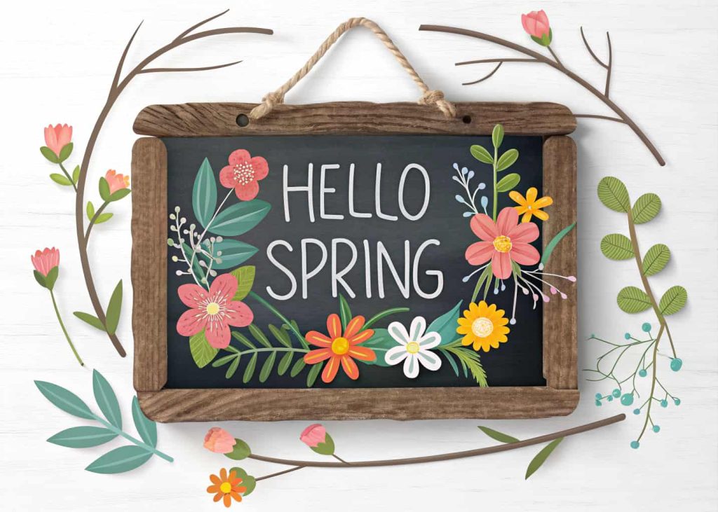 Chalkboard spring door hanger with “Hello Spring” written on it and decorated with flowers and greenery.