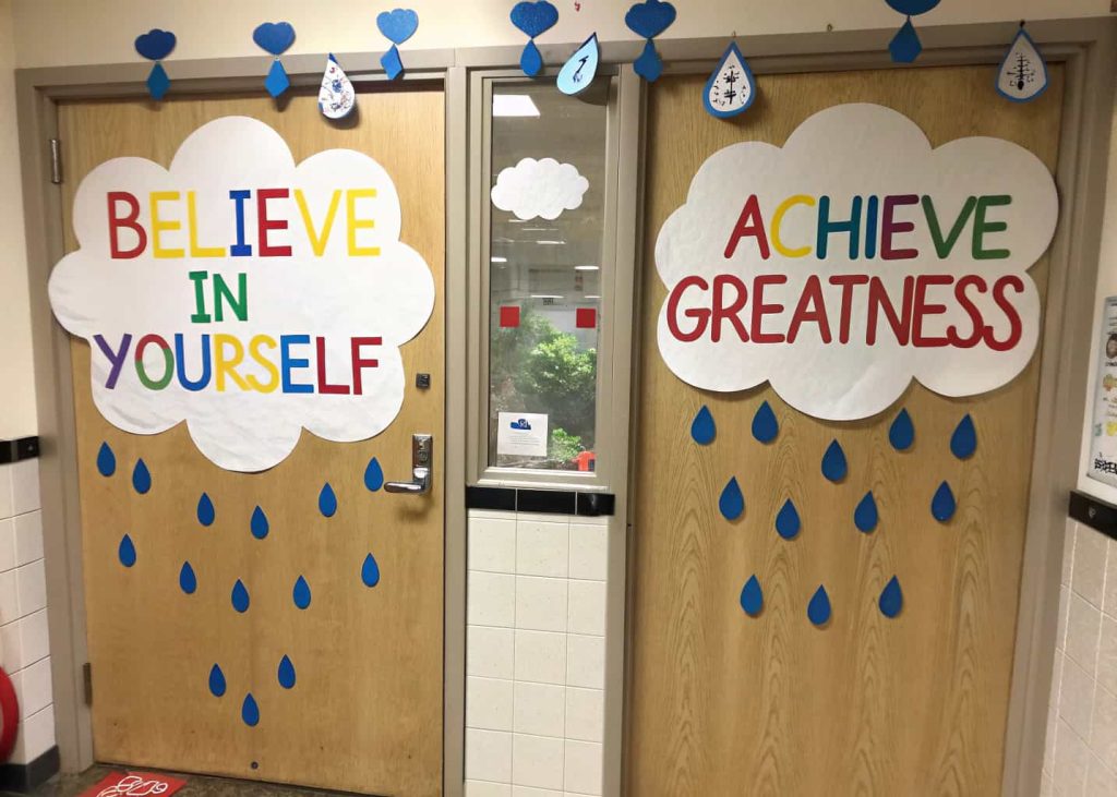 Classroom door with white paper clouds and blue raindrops, featuring motivational messages.