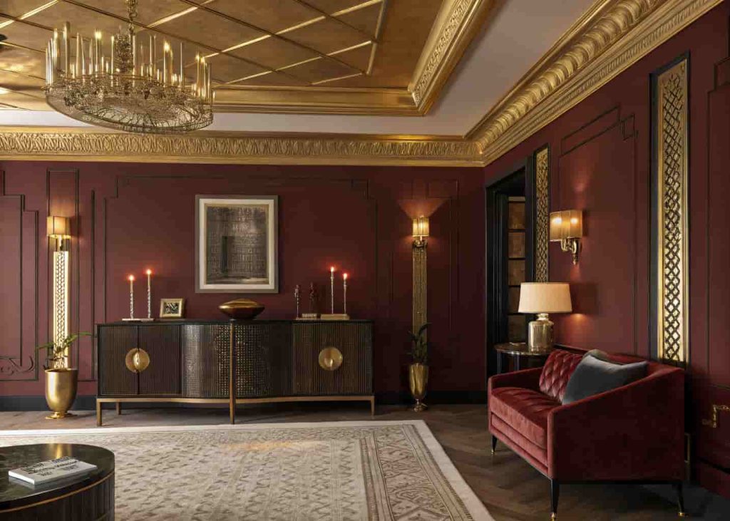 Art Deco living room with gold leaf ceiling details, brass accents, and warm vintage lighting against deep-toned walls.
