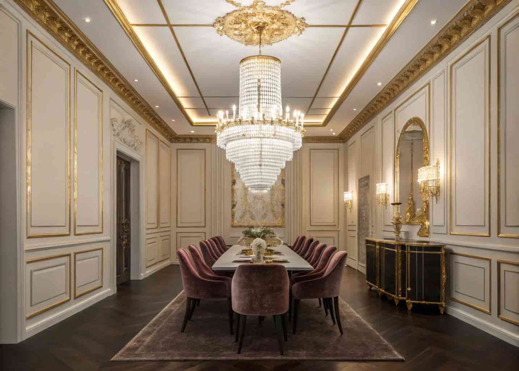 Grand crystal chandelier illuminating an Art Deco dining room with gold wall trim, dark floors, and velvet seating.