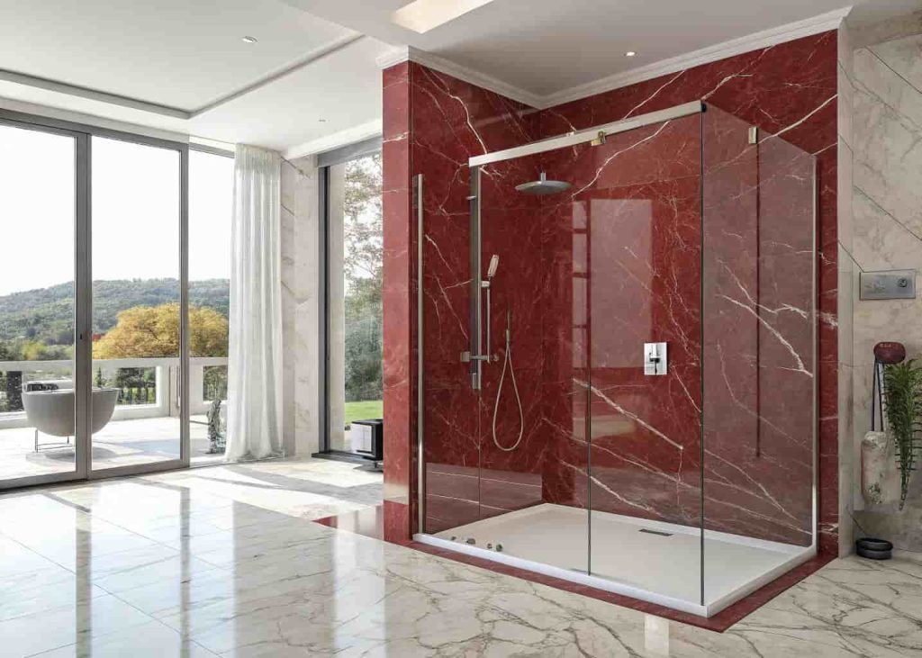 Red marble shower with frameless glass enclosure and rain shower head in a modern designer bathroom.