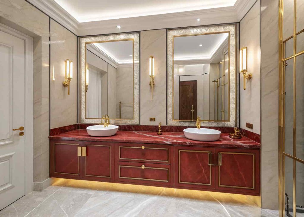 Red marble double vanity in a master bathroom with gold fixtures and large mirror for an elegant designer look.