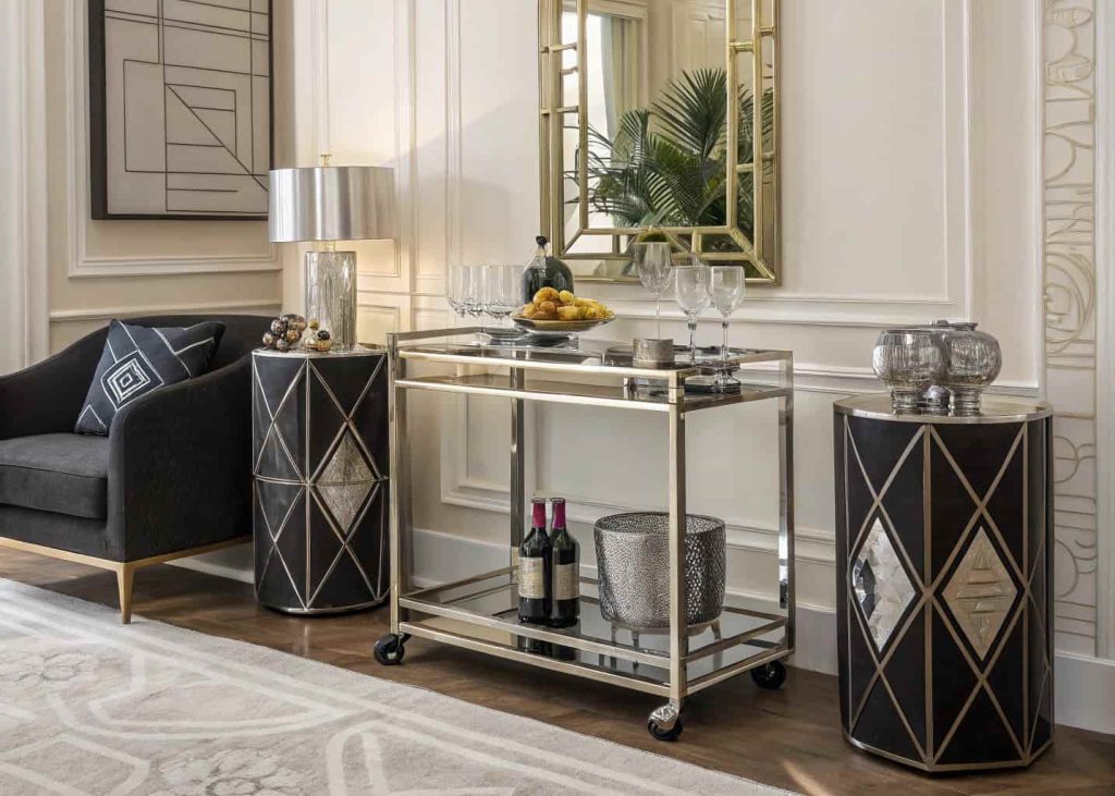 Art Deco living room corner with a chrome and glass bar cart, geometric glassware, and a mirrored wall backdrop.