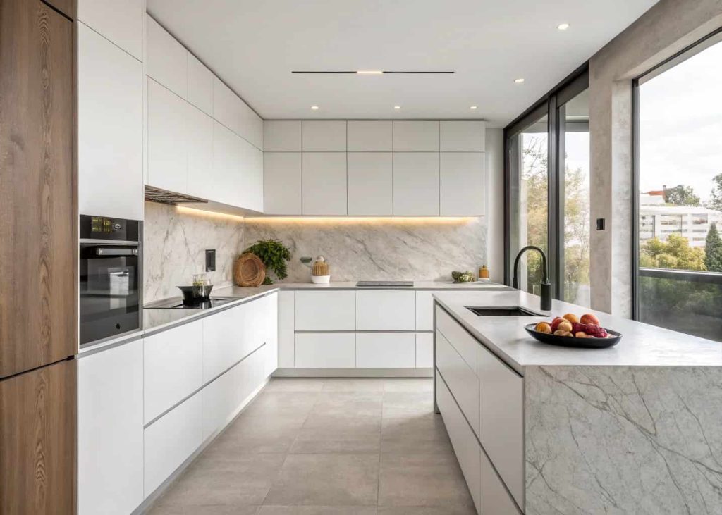 A sleek minimalist kitchen with stone countertops, handleless cabinets, and a single bowl of fruit as the only visible decoration
