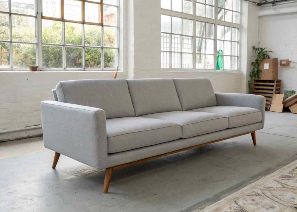 Real photo of minimalist living room with a low-profile mid-century modern sofa in grey or olive, clean straight lines, simple wooden legs, uncluttered room, natural light, no decorative detailing