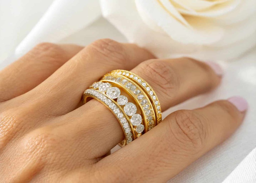 Three layered yellow gold bands of different widths stacked together on a ring finger against a soft white background