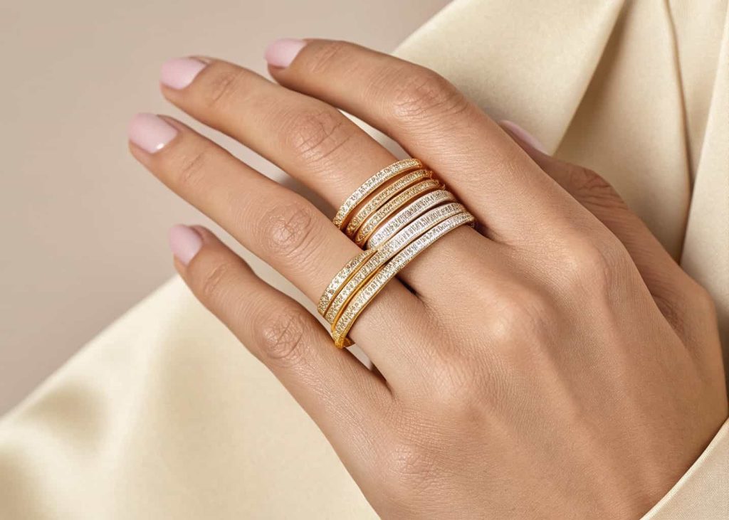 Mixed metal stacking rings in yellow gold, white gold, and rose gold worn together on a woman's finger against a neutral background.