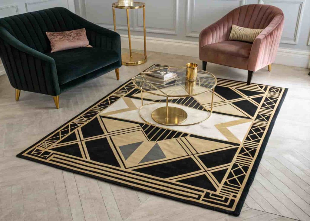 A large black and gold geometric rug anchoring a Neo Deco living room with velvet chairs and a brass coffee table