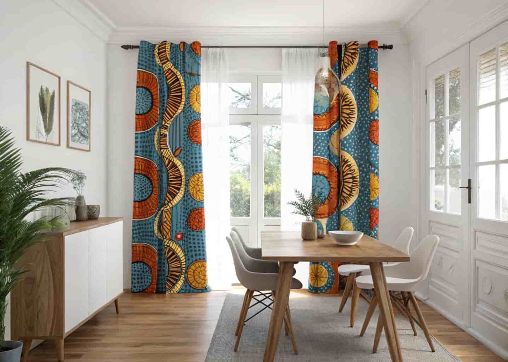 Vibrant floor-length Ankara wax print curtains in blue and orange bold patterns hanging in a bright modern dining room with wooden furniture