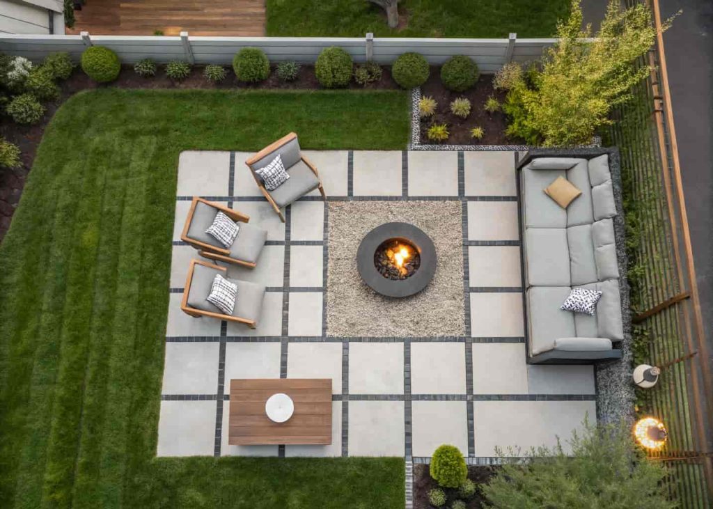 Overhead view of a modern backyard fire pit lounge with large concrete pavers as the base, crushed gravel border, and modern outdoor furniture.