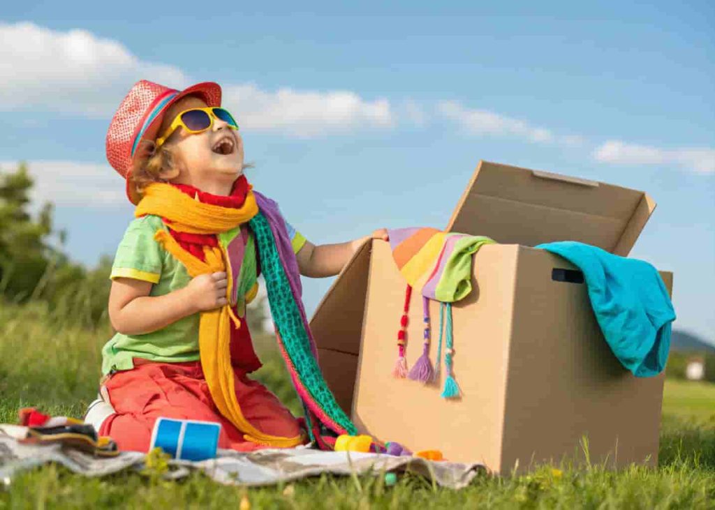 Preschooler playing dress-up with creative costume box as summer imaginative play activity