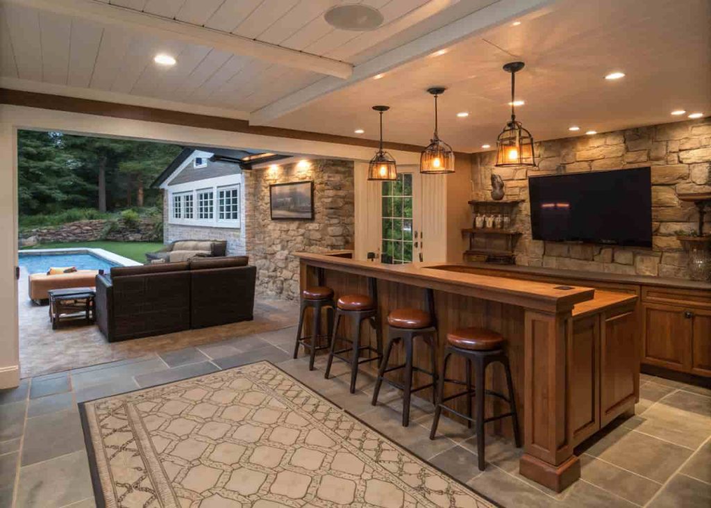 A detached garage transformed into a home bar and entertainment space featuring a built-in bar, bar stools, large TV, pool table, and warm Edison bulb lighting