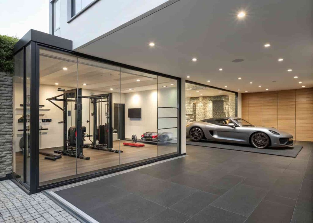 A luxury garage-gym combo space with a frosted glass divider separating the gym side from the car display area