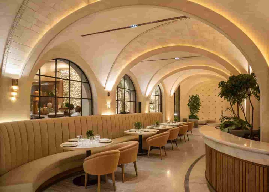 Modern restaurant interior featuring curved arched doorways, rounded booth seating, and sculptural plaster walls in warm cream tones creating a soft organic atmosphere.