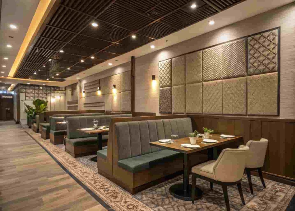 Modern restaurant interior featuring acoustic design elements including upholstered booths, fabric wall panels, and area rugs to create a comfortable and noise-controlled dining environment.