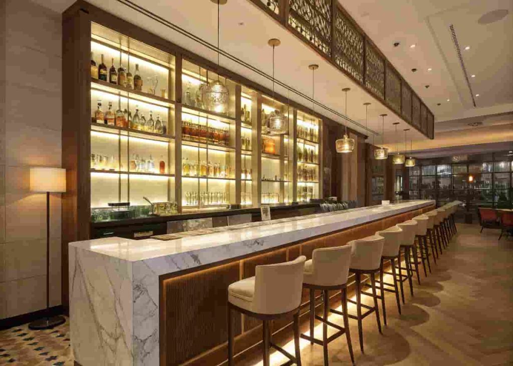 Elegant restaurant bar counter with backlit bottle display and marble countertop under ambient lighting