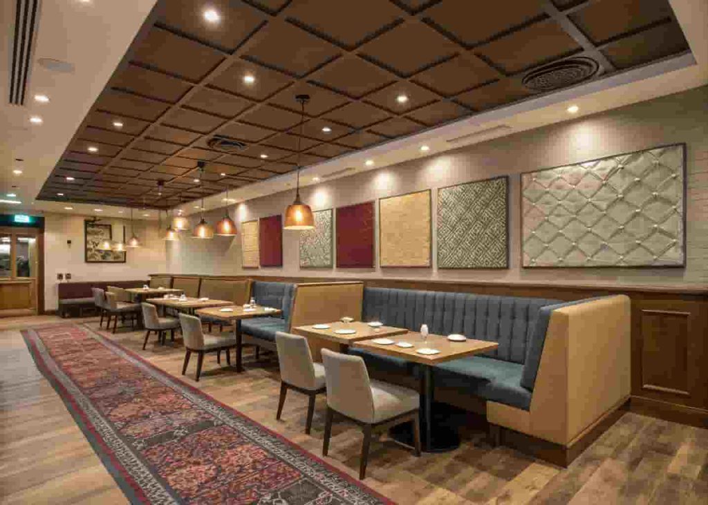 Restaurant interior with acoustic ceiling panels, upholstered seating, and rugs for sound absorption