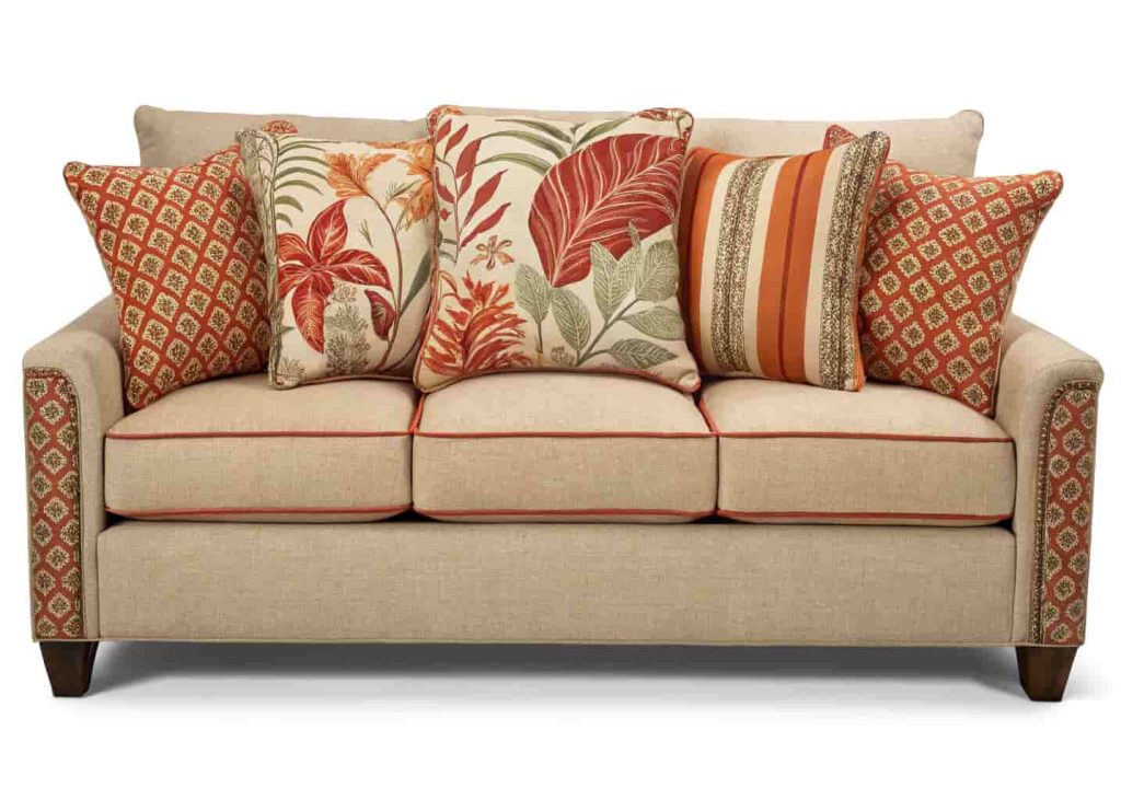 A maximalist sofa with three patterned cushions in varied scales, botanical, stripe, and geometric, sharing warm rust and cream tones.