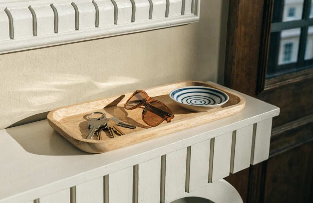 A wooden tray on a console table holding keys, sunglasses, and a small dish, neat and organized