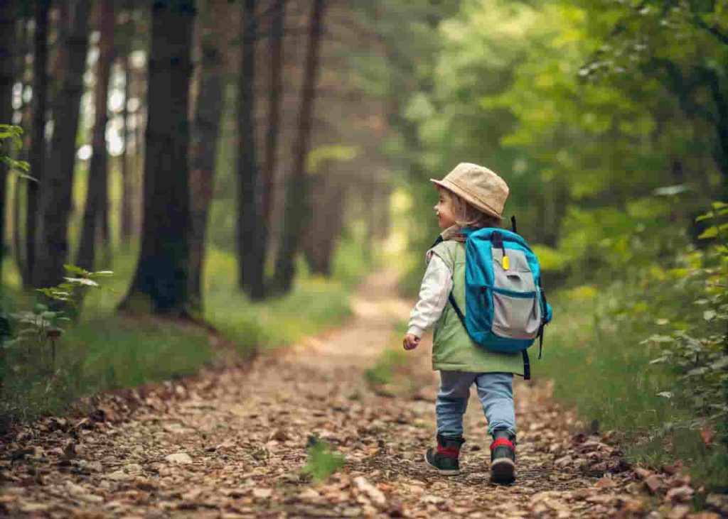Child hiking on a wooded trail with a backpack, exploring nature as a summer activity