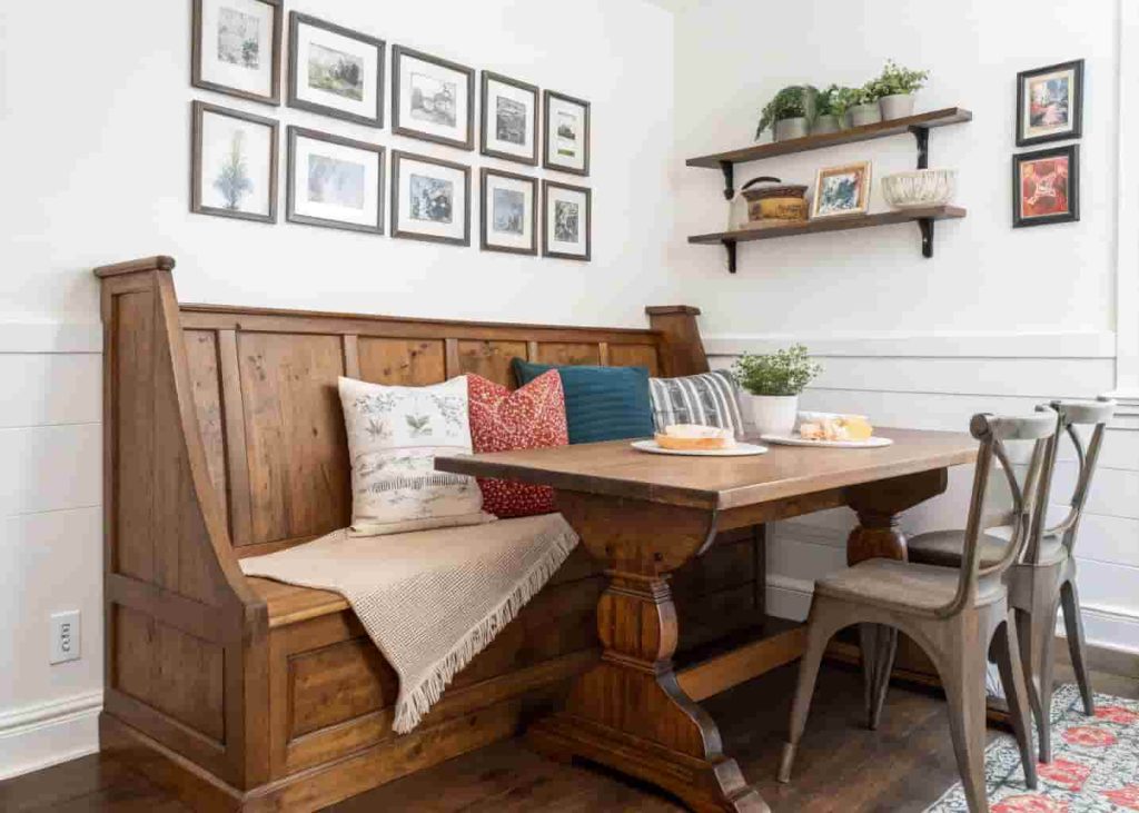 Repurposed church pew breakfast nook with farmhouse table and gallery wall in a cozy kitchen dining area