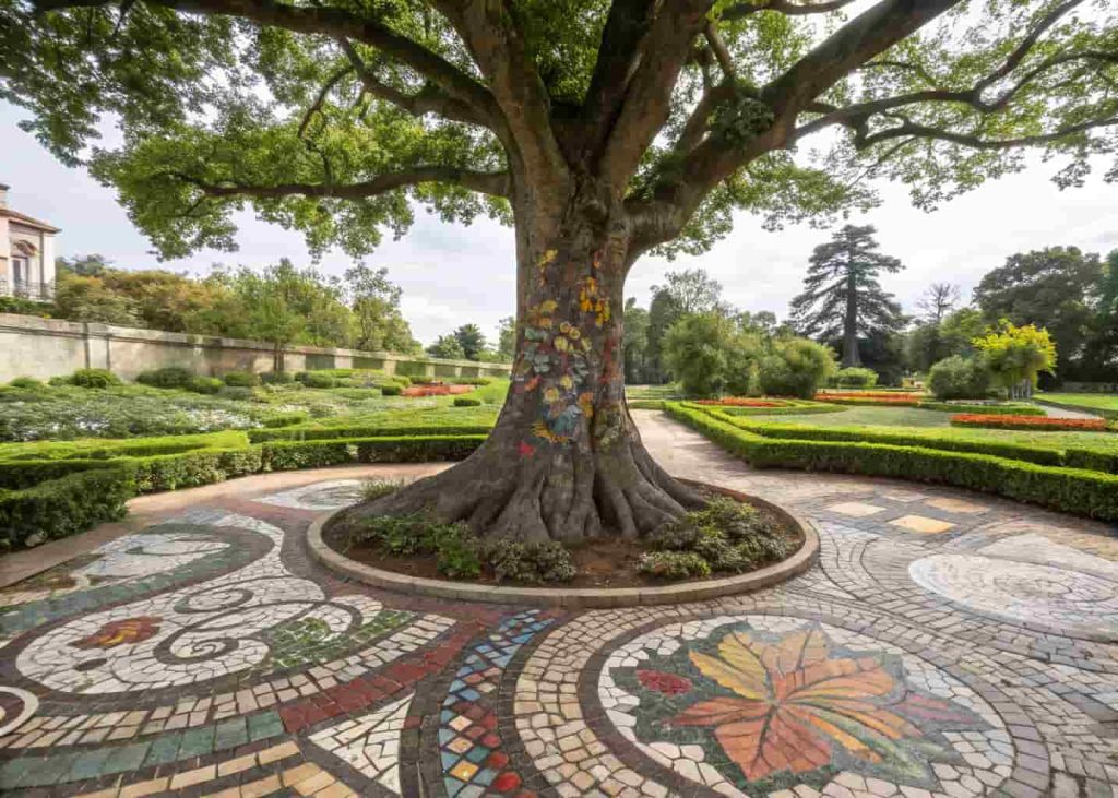 Colorful mosaic tree surround with ceramic tile designs at base of garden tree