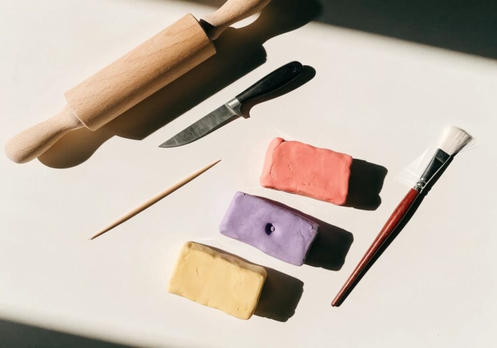 Flat lay of clay crafting tools including rolling pin, sculpting knife, and colorful clay blocks