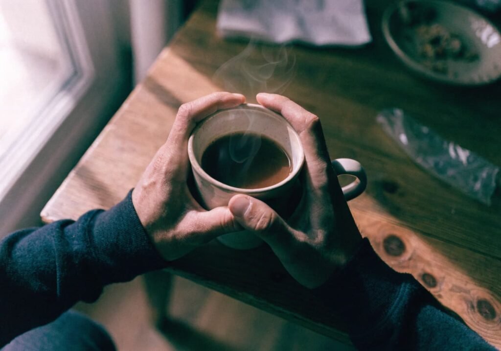 Hands holding a warm coffee cup on a wooden cafe table with soft natural light