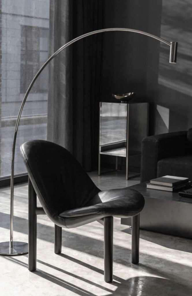 Chrome arc floor lamp curving over a leather chair in a modern living room