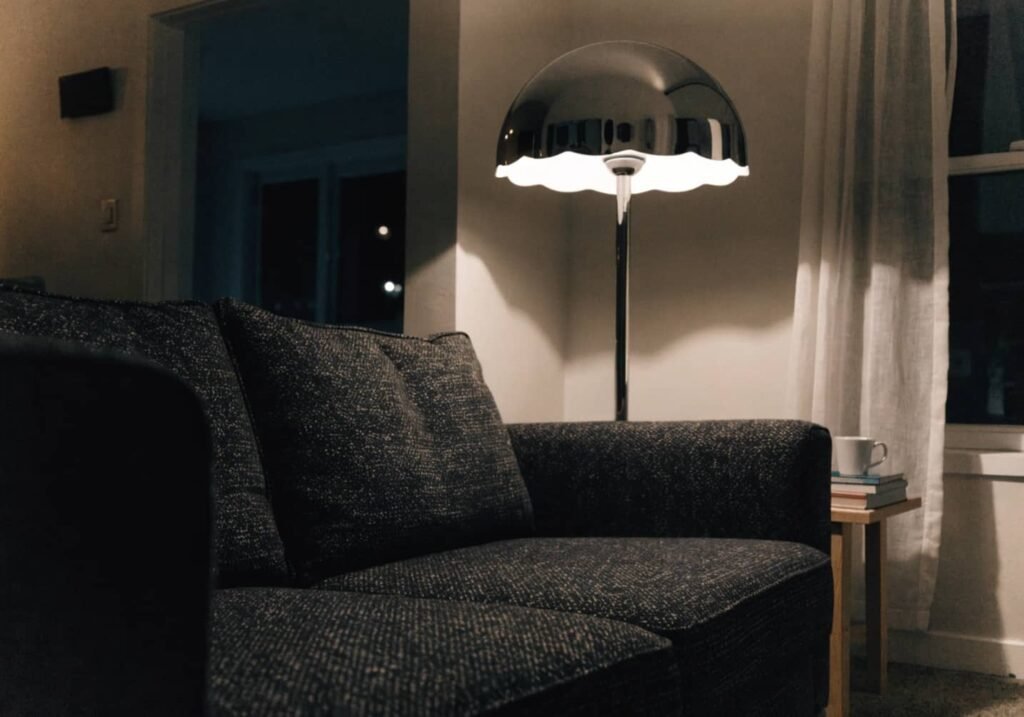 Chrome floor lamp glowing softly behind a living room sofa
