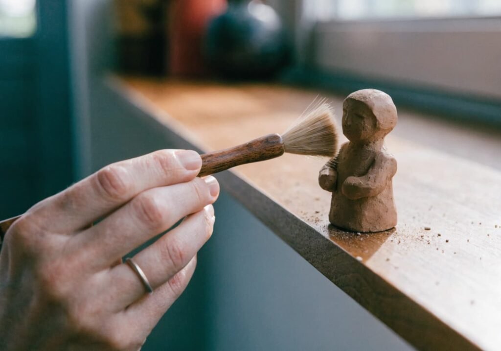 Gently dusting a small clay figure with a soft brush