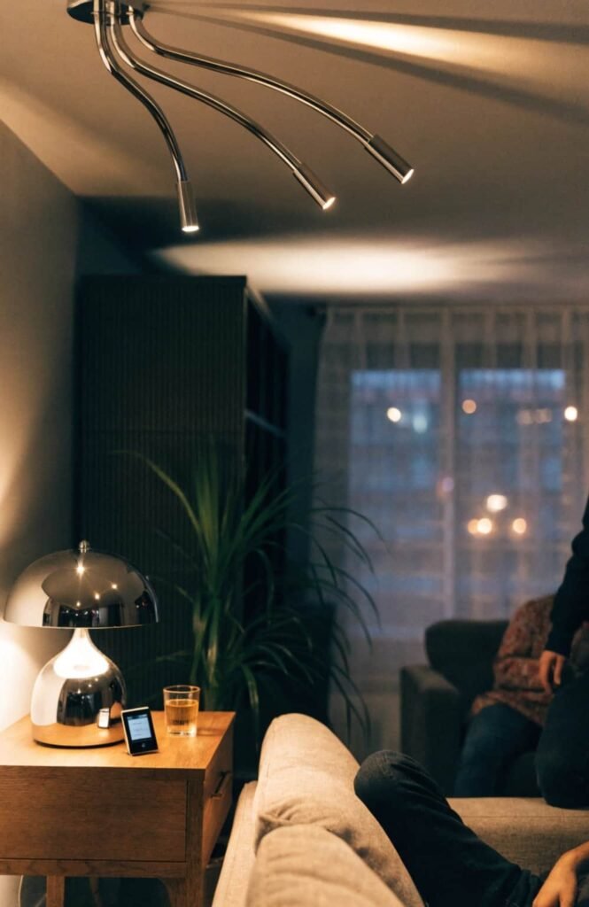 Brushed chrome ceiling fixture and table lamp creating layered lighting in a modern living room