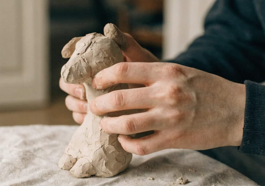 Beginner hands shaping a small air-dry clay figure at home
