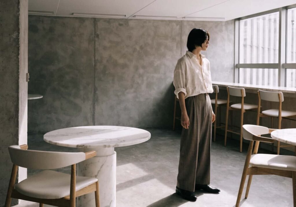 Minimalist linen shirt outfit in a modern cafe with concrete walls and marble tables.