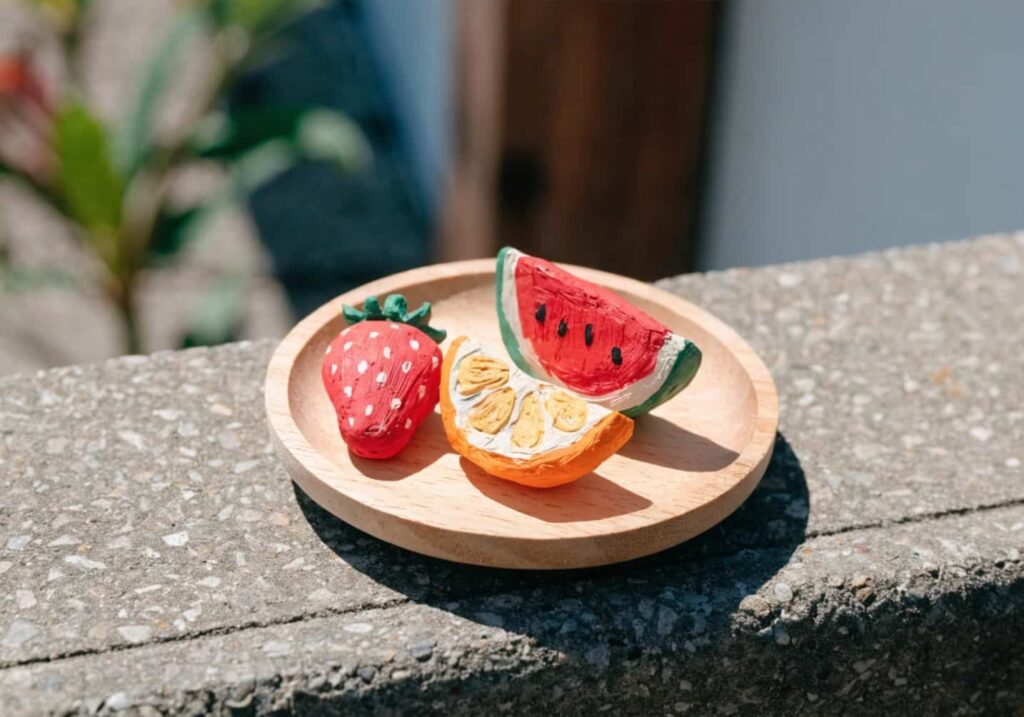 Miniature clay fruit figures including strawberry and watermelon slice on a wooden tray