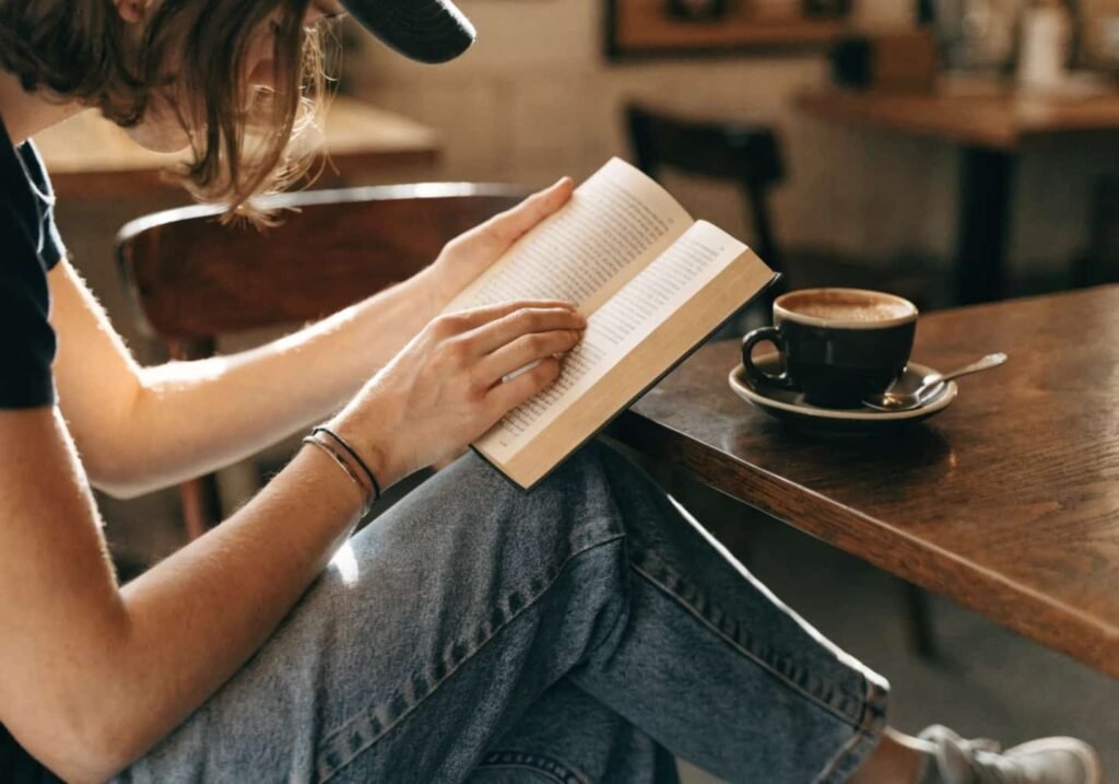 Person casually reading a book at a cafe table.