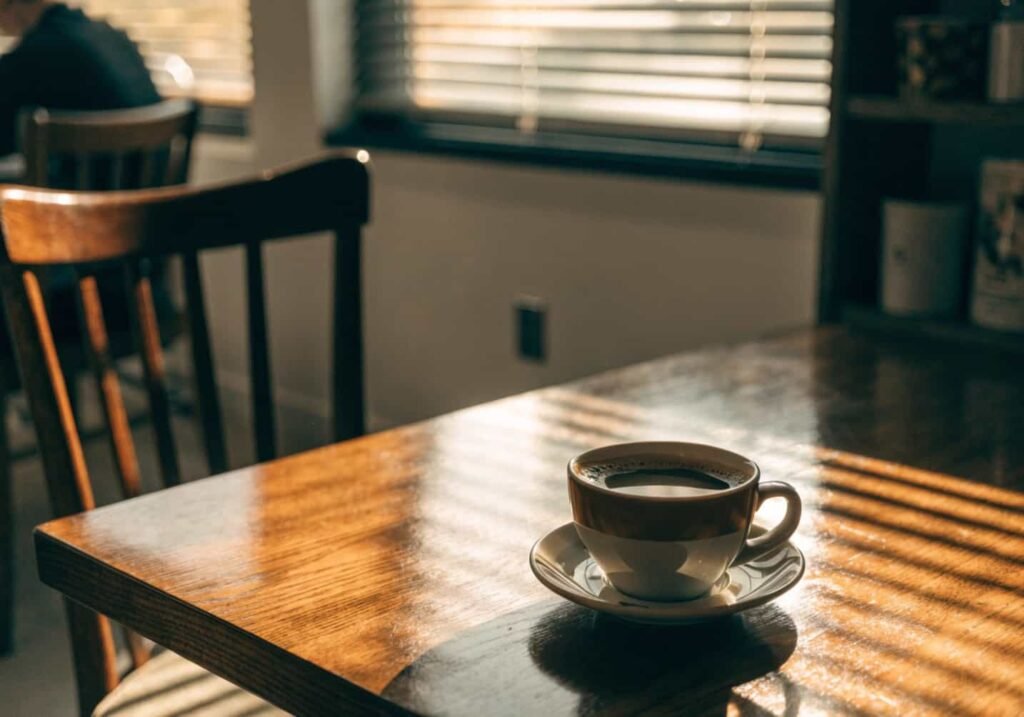 Soft shadow lighting from window blinds across coffee cup in aesthetic cafe