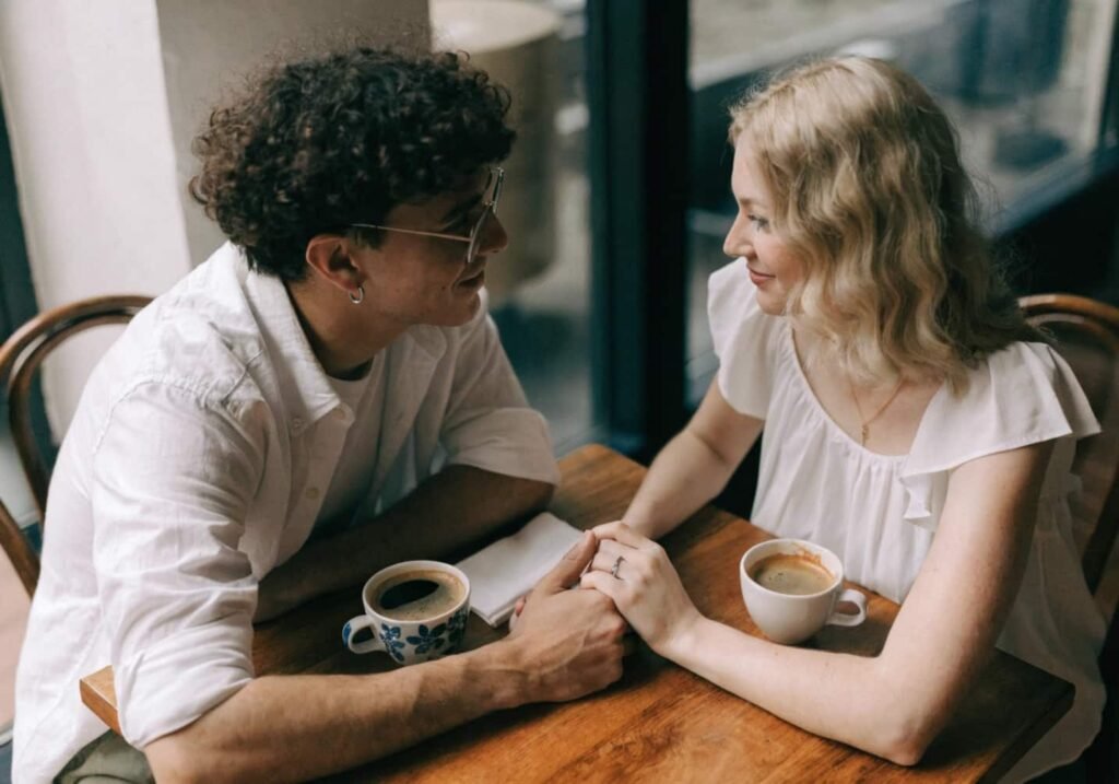Couple holding hands across a cafe table with coffee cups nearby