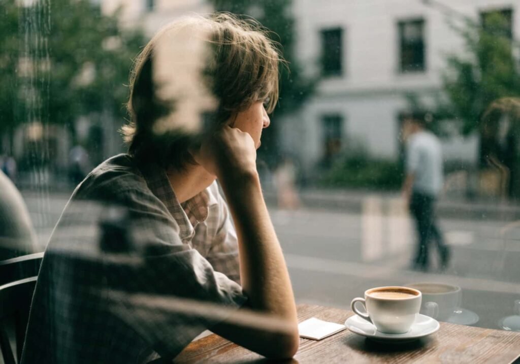 Person resting chin on hand looking out a cafe window in a candid dreamy pose.