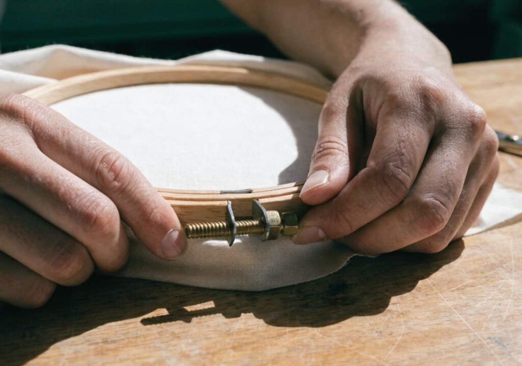Hands stretching cotton fabric into a wooden embroidery hoop before stitching
