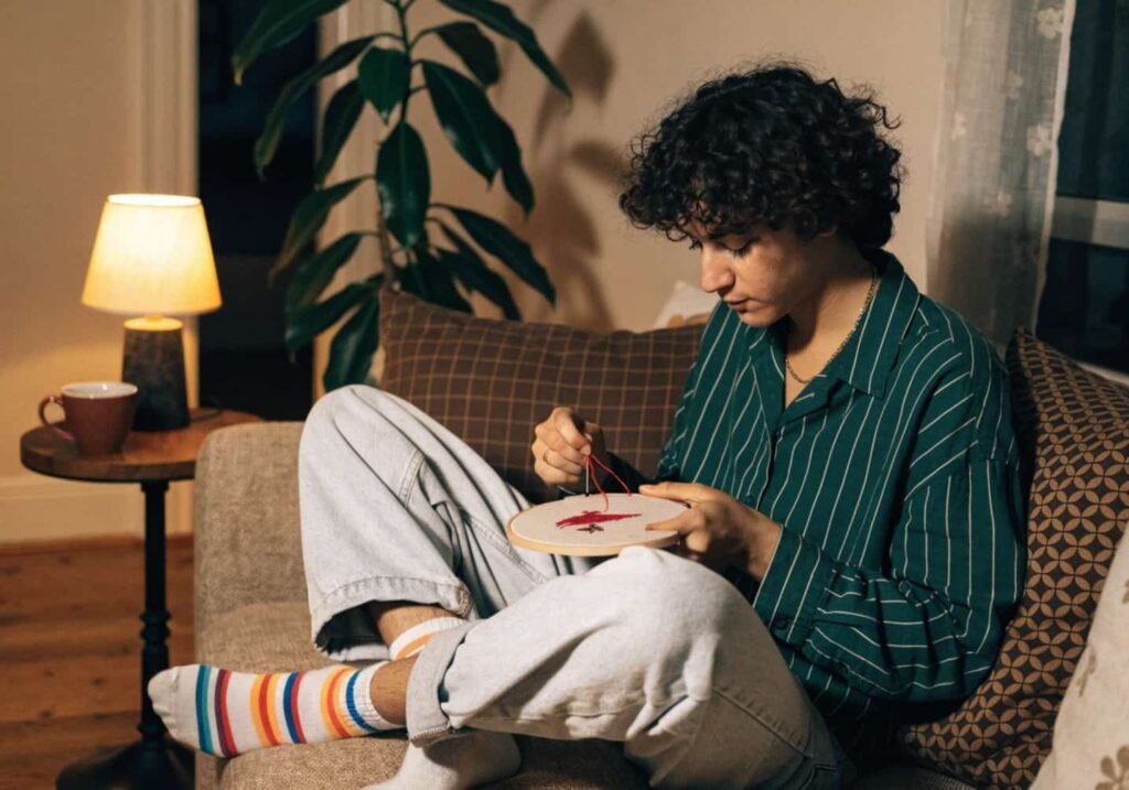 Person relaxing on a couch while stitching an embroidery project in the evening