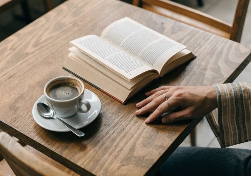 Coffee cup with an open book and hand wearing a ring on a wooden table