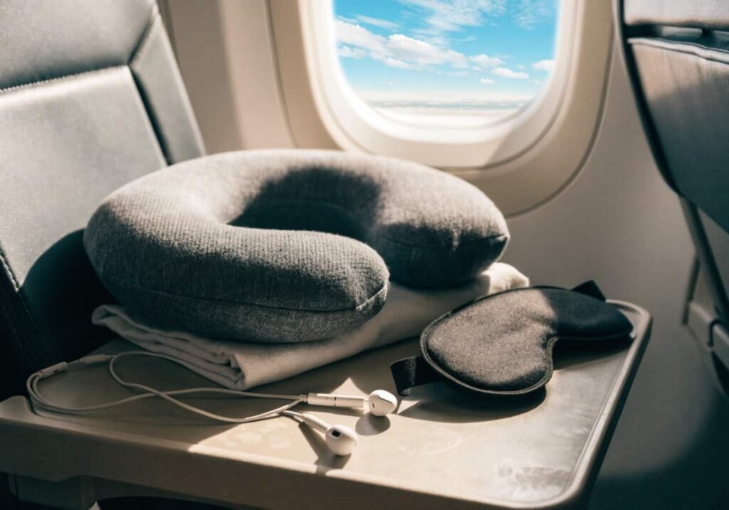 Neck pillow, eye mask, and earphones set up for comfort during a long flight.