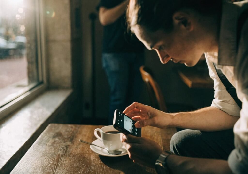 Person adjusting phone camera settings to photograph coffee on a cafe table