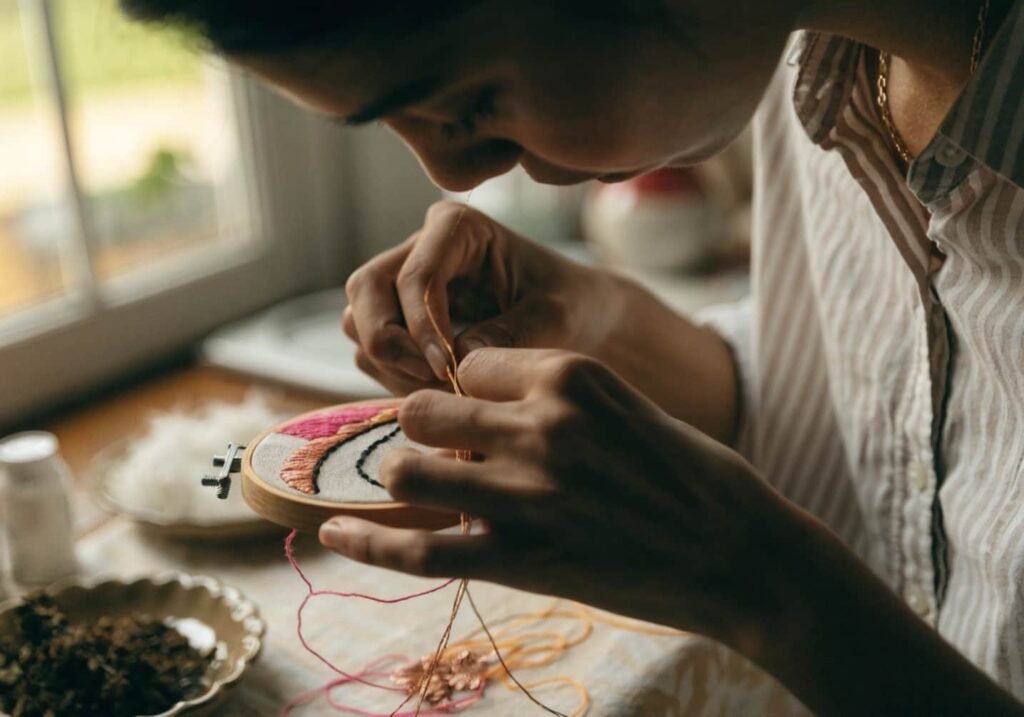 Person hand-stitching an embroidery hoop using colorful and metallic threads