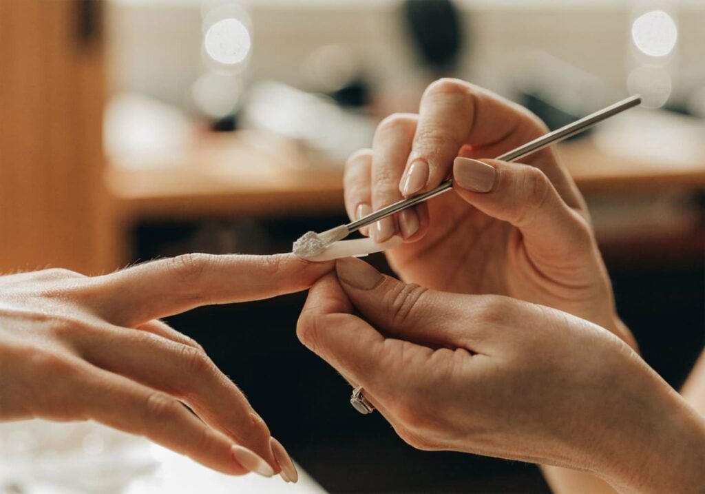 Nail technician applying acrylic powder and liquid monomer to shape a nail extension.