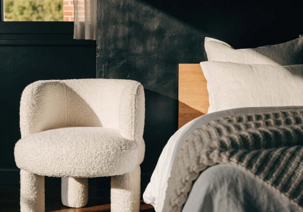 Cream boucle armchair and knit throw softening a black bedroom wall for a cozy feel