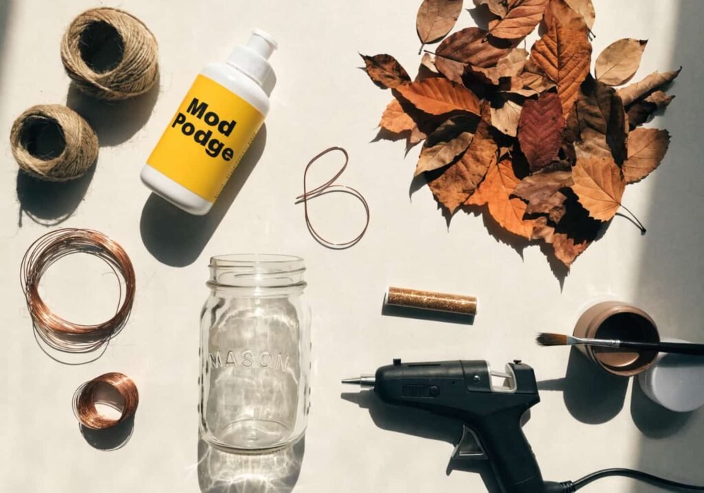 Craft supplies laid out for making fall mason jar centerpieces including twine, glue, and dried leaves