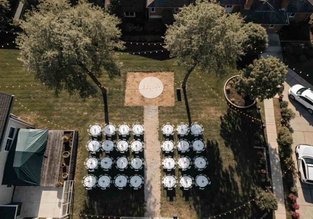 Backyard space arranged for a casual wedding reception with tables and string lighting.