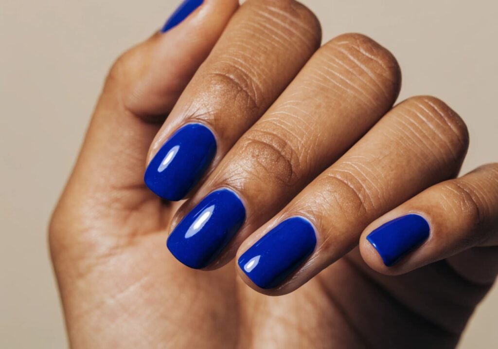 Hand with glossy cobalt blue nail polish on neutral background